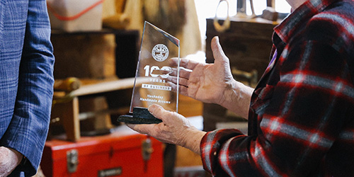 A man holds a glass plaque noting 100 years of business.