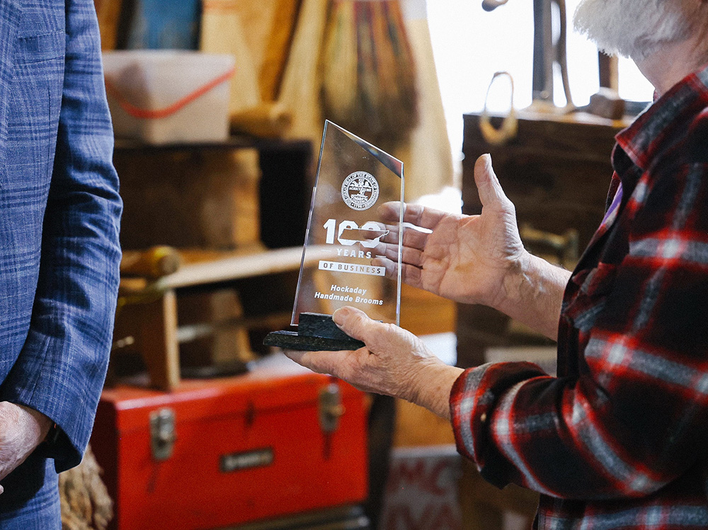 A man holds a glass plaque noting 100 years of business.