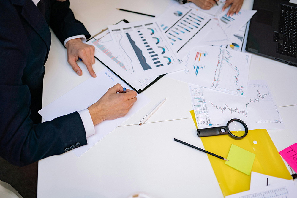 Two people sit at a desk and work on finance documents.