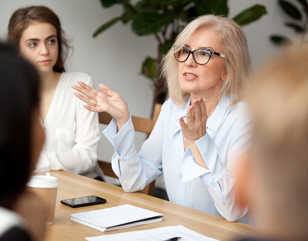 A woman leads a discussion between a group of people at a conference table.