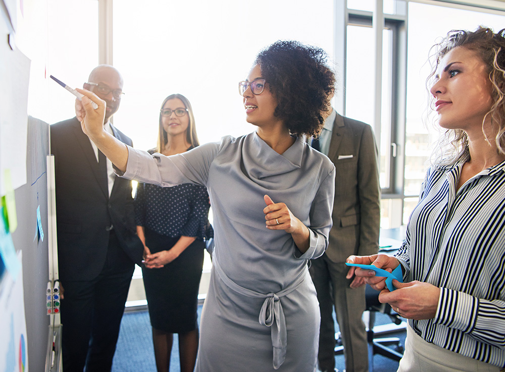 A woman leads a group discussion around a display board.