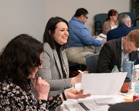 A smiling woman sits in a small group talking with others at a conference.