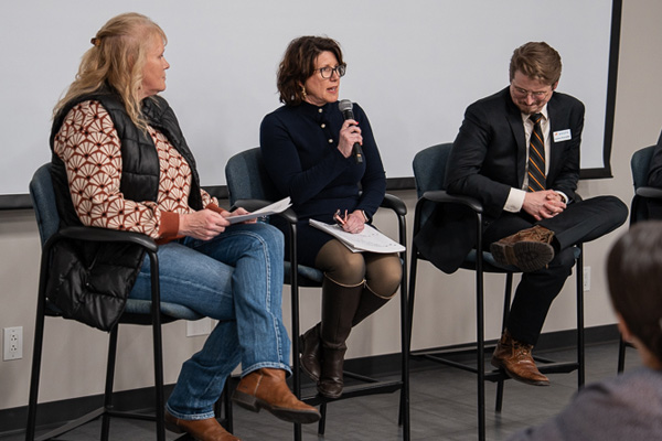 A woman with a microphone speaks from a panel of guest speakers.